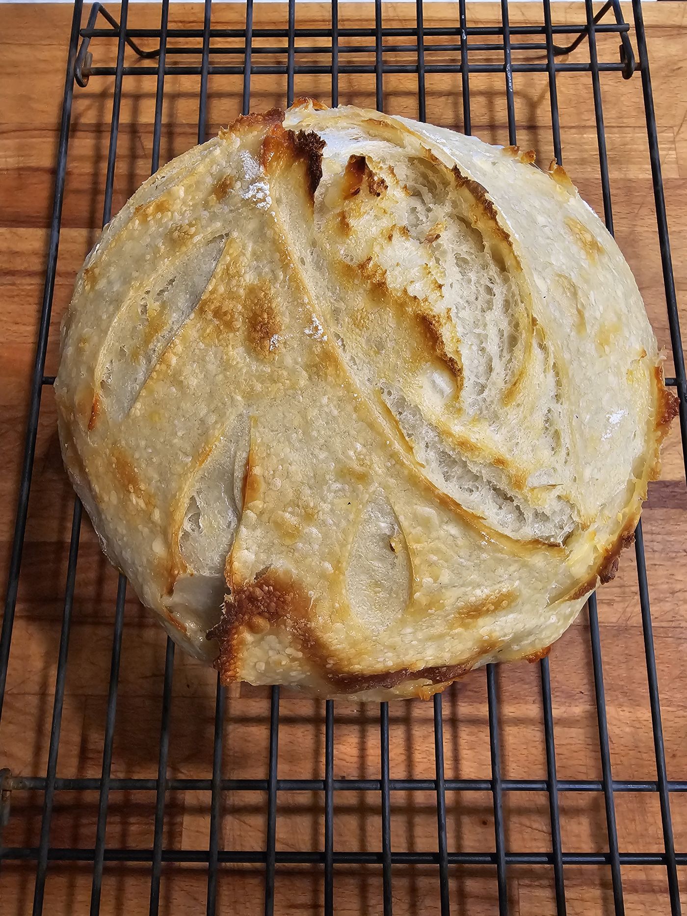 A loaf of homemade sourdough bread cooling on a rack